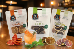 Three packages of dried citrus fruits with a glass of orange juice on a wooden surface.