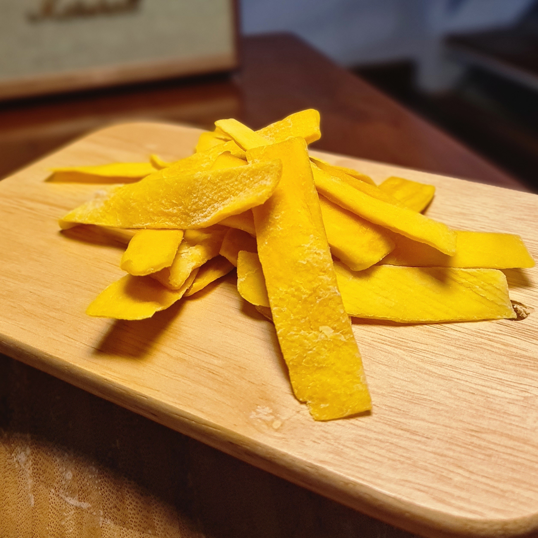 Yellow dried mango strips on a wooden cutting board