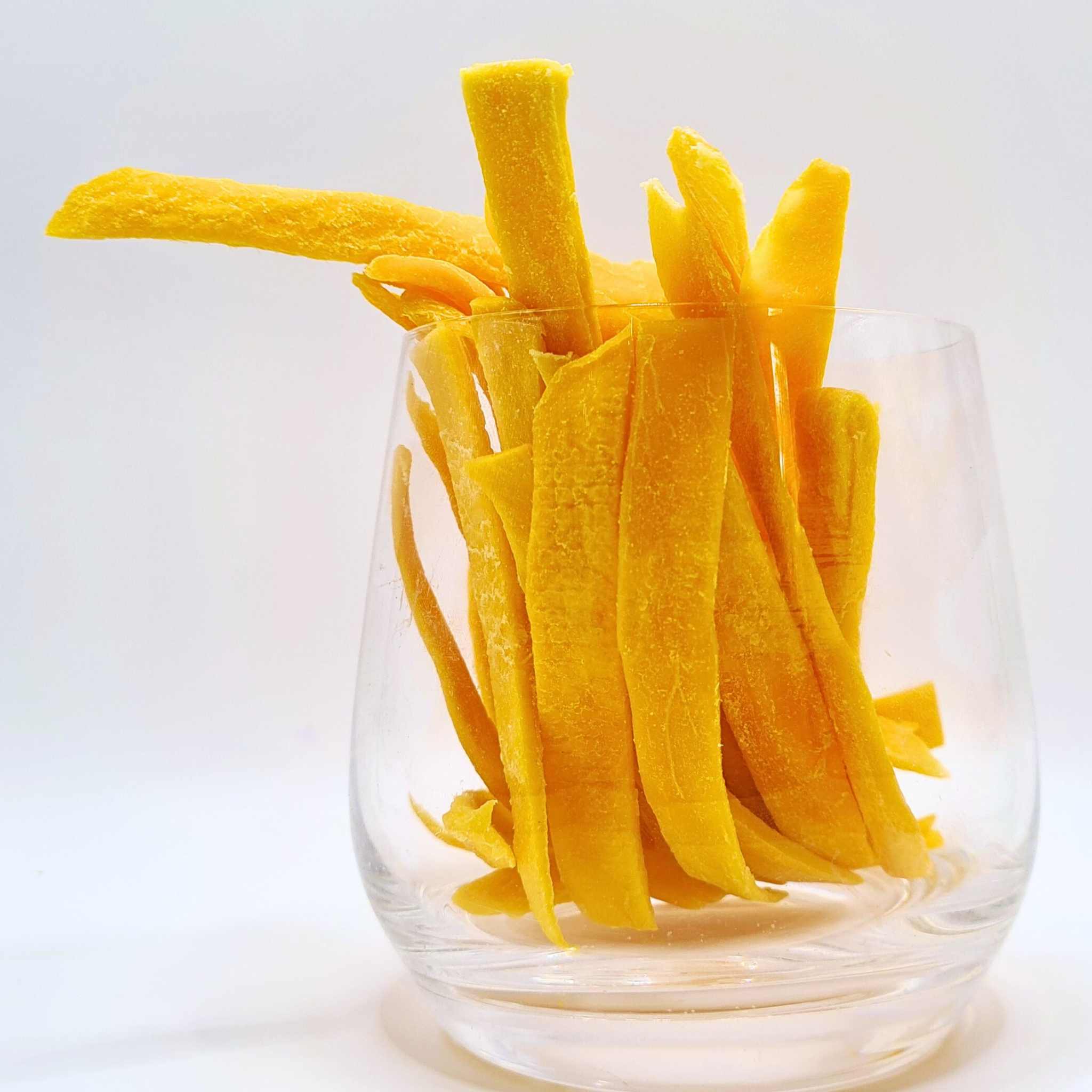 Clear glass filled with yellow dried fruit on a white background