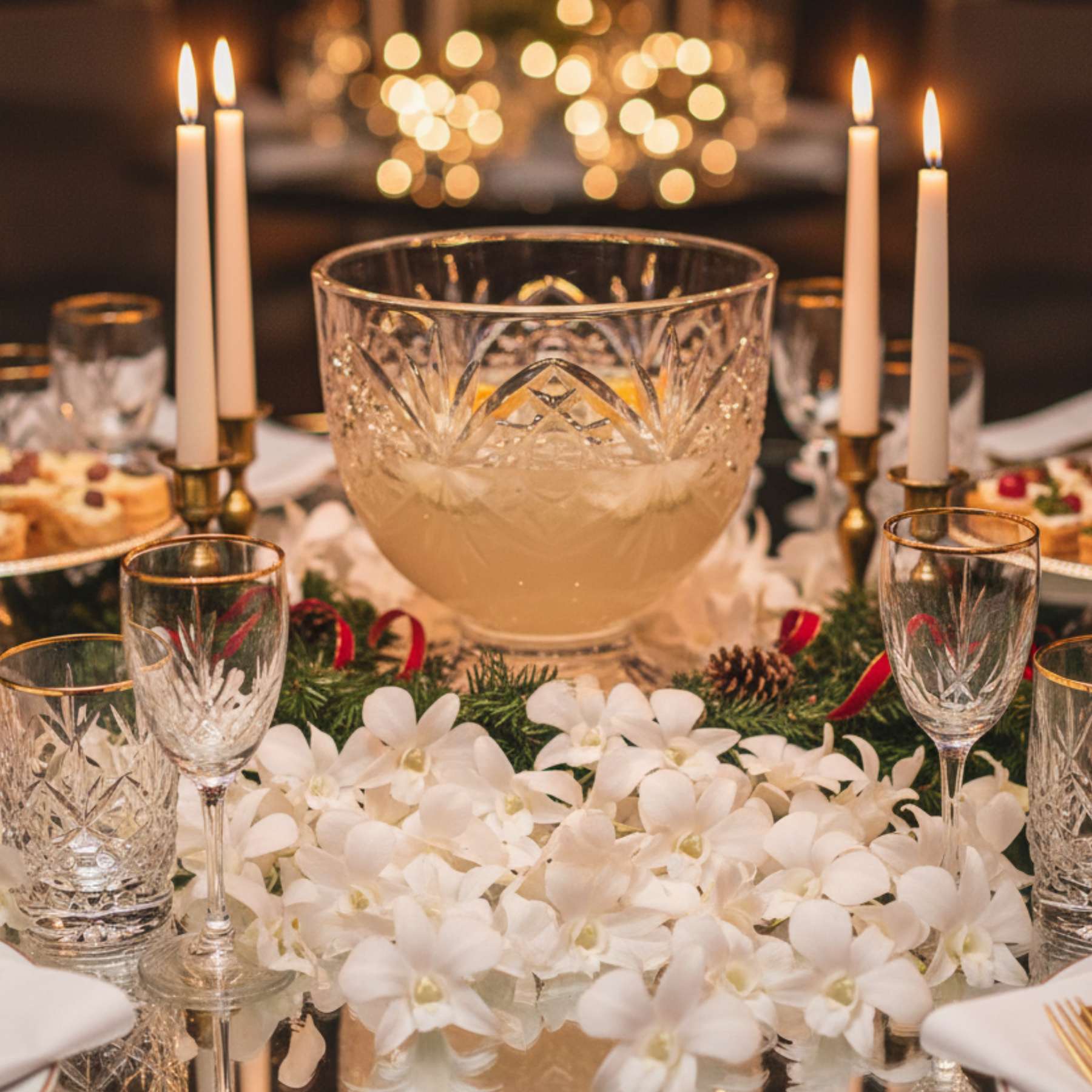 Decorative table setting with crystal glasses, a bowl, and white flowers on a blurred festive background.