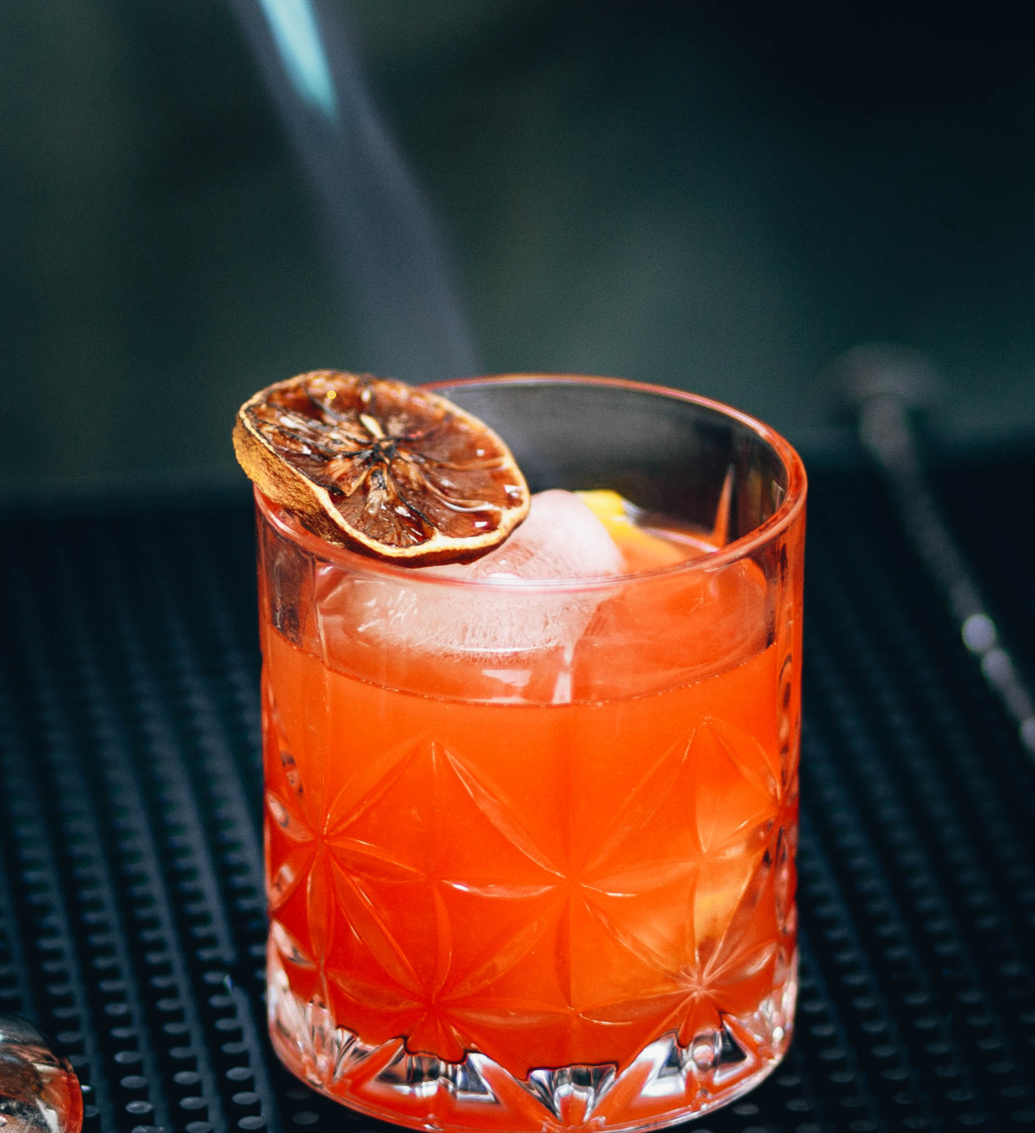 Bartender adding dried fruit and mint garnish to a handcrafted orange cocktail, ideal for mixology or upscale bar presentation.